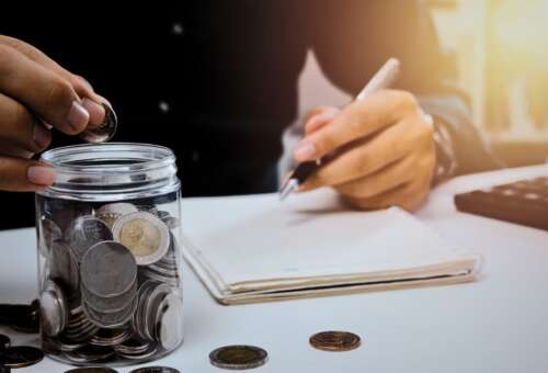 man in suit, white table, pen, coins, book, sunlight, jar of coins